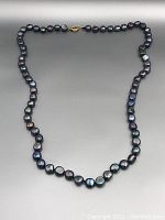 Full view of the Tahitian black pearl necklace laid out showing the shape and color of the pearls, and gold clasp.