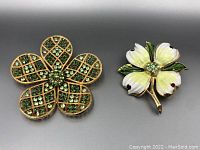 Two floral brooches side by side on a gray background, showing detail of rhinestones and enamel colors.