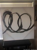 Full view of abstract artwork showing large black circular brush strokes on white canvas with some natural light from window blinds in background.