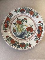 Top-down view of one decorative plate showing central floral and fruit motif with red flowers and blue basket-like element.