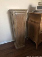 Side view of wooden pedestal showing tapered paneled design and natural wood finish.