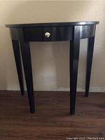 Front view of wooden demi lune console table showing drawer with brass knob and tapered legs.