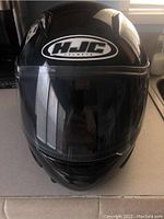 Front view of black HJC full face motorcycle helmet with clear visor showing the HJC logo on the forehead area.
