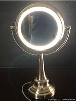 Front view of the lighted magnifying mirror with LED light ring illuminated and showing the regular mirror side reflecting surroundings.