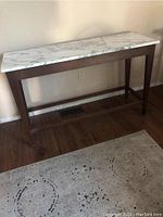 Front view of the wooden sofa/console table with white marble top showing its full length and wooden legs.