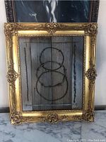Framed gold ornate frame containing mounted antique barbed wire collection on barn wood mounting. Overall view of lot.