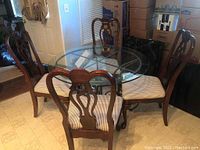 Round glass top table with metal base surrounded by four wooden Queen Anne style chairs with striped upholstery.