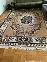 Full view of the rectangular area rug laid on wooden flooring, showing the central medallion and floral border.