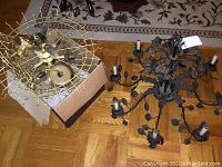 Photo showing both fixtures; brass and white globe light with brass cage, and black metal chandelier with flower and leaf detailing.