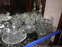 Photo displaying various clear crystal and cut glass bowls, cake stand, basket, and drink glasses arranged in a display cabinet.