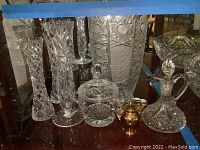 Various crystal glass vases, sugar bowl, cruet with stopper, and mini gold ceramic tea set on surface