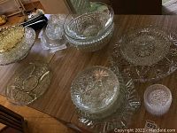 Various cut glass bowls, coasters, serving trays, including amber bowl and a fish-shaped tray on wood table.