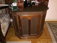 Front view of one hexagonal wooden end table with cabinet door and items on top.