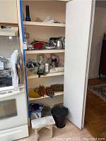 Kitchen cabinet shelves holding kitchenware items including teapots, graters, a blender, a crab pot, and a small white stool.