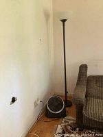 Black metal base torchiere lamp and black plastic floor fan in corner of room near wall and couch, plugged in but untested.