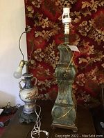 Photo showing two table lamps. One ceramic with exposed light bulb socket, no shade. One tall greenish distressed lamp without shade and with electrical cord wrapped.