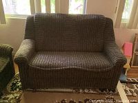 Front view of black and tan textured upholstered loveseat with fixed seat and back cushions. Rounded arms and pleated skirt cover the bottom edges.