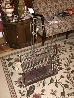 Photo showing both magazine and quilt racks positioned on a floral rug. Magazine rack has metal and woven reed basket. Quilt rack is metal with scrollwork and horizontal bars.