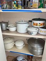Shelf with various vintage metal pots including enamel floral printed pots and plain aluminum pots.