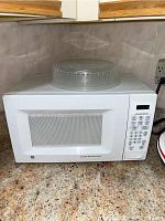 Front view of white GE microwave model JES738WJ02 sitting on granite countertop surrounded by tiled backsplash, showing the mesh door and ventilation top.