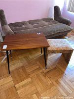 Wooden table and upholstered stool placed in front of sofa on wooden parquet floor.