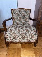 Front view of vintage upholstered armchair showing floral fabric and carved wood frame.