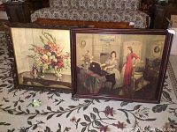 Photo showing two framed prints on board, one floral and one interior scene, placed on patterned cloth.
