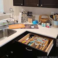 Overview of kitchen counter with two-tier dish rack, wooden basket, knife block with knives, blue butter dish, small jars, and towel rack visible