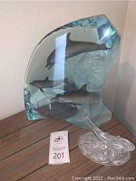 Large blue glass dolphin sculpture and smaller clear dolphin sculpture on wooden surface