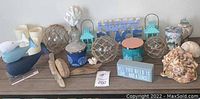 Front view of tabletop displaying ocean and beach themed decor including whale figurines, candles, driftwood, glass fishing floats, coral bottle, lanterns, shells, and signs.