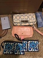 Photo showing four small wallets and wristlets of different patterns and materials laid out on carpet.