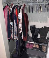 View of metal clothing rack with assorted women's clothes hanging and shoes on shelving beneath