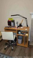 Full view of desk setup including wooden desk, white office chair, desk lamp, and scattered office supplies on desktop and shelves.