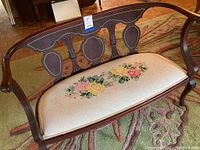 Full view of the antique English mahogany settee showing carved wooden back and needlepoint upholstered floral seat.
