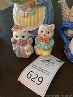 Porcelain cat figurines with pastel colors and detailed outfits, part of collectible cat tea set.