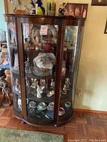 Full front view of dark wood china hutch with curved bevelled glass front door and side panels filled with display items.