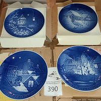 Four Bing & Grondahl Christmas collector plates displayed in their original boxes with blue and white winter scenes on each plate