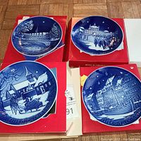 Overview photo showing all four Bing & Grondahl collector plates in their red boxes with title and year visible on the plate rims.