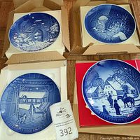 Four blue and white collector plates in original packaging, showing winter and Christmas scenes in detailed artwork.