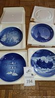 Four Bing & Grondahl collector plates in white protective boxes, featuring blue and white winter and Christmas-themed designs.