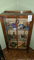 Front view of wood and glass china cabinet with decorative scrollwork on glass doors and miscellaneous items inside.