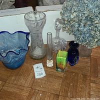 Wide view of lot showing all items including crystal decanter, various small colorful vases, and dried blue hydrangea.