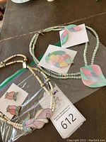 Photo of two sets of necklaces and earrings, one cream/tulip motif and one mint/shell motif, laid out on table.
