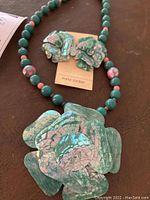Necklace and matching earring set with large flower-shaped stone overlay on necklace and earrings with green beads and pink spacer beads.
