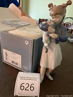 Porcelain figurine of a young girl holding a cat, standing beside the original box with label.