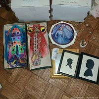 Photo showing Barbie collector plate, boxed Japanese kites with colorful face designs, two framed silhouette art pieces, and a small figurine on a parquet floor.