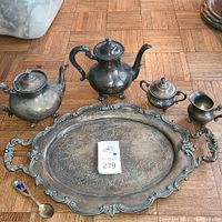 Full view of the 7-piece Reed & Barton silver plated serving set including platter, teapot, coffee pot, creamer, sugar bowl, and spoon on wooden floor showing tarnish.