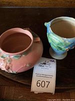 Two Roseville pottery vases; one apricot green ombre short vase and one taller blue and tan grape leaf motif vase placed on wooden surface with auction lot tag 607