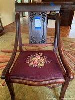 Front view of the vintage wooden armchair showing floral needlepoint seat and carved backrest with relief detailing