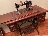 Full view of vintage Axis treadle sewing machine mounted in wood cabinet with drawers and treadle pedal.